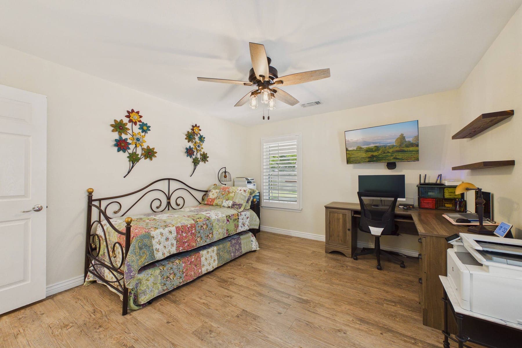 The second bedroom set up with a patchwork-quilted daybed on one side and a desk with a monitor, printer and shelving on the other.