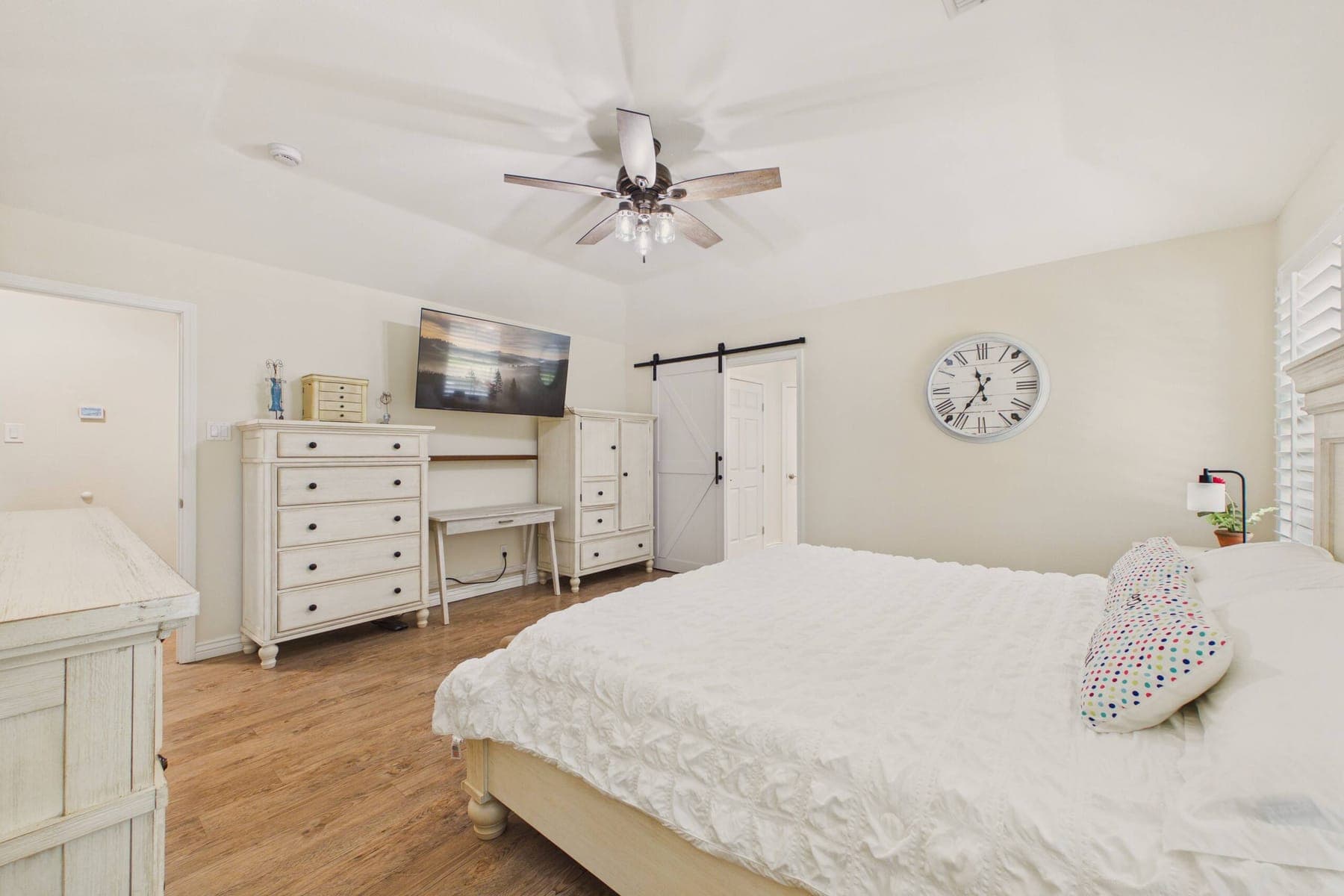 The third bedroom: a large bed with a white textured cover, a wall-mounted television above a writing desk, painted timber furniture and a sliding barn door.