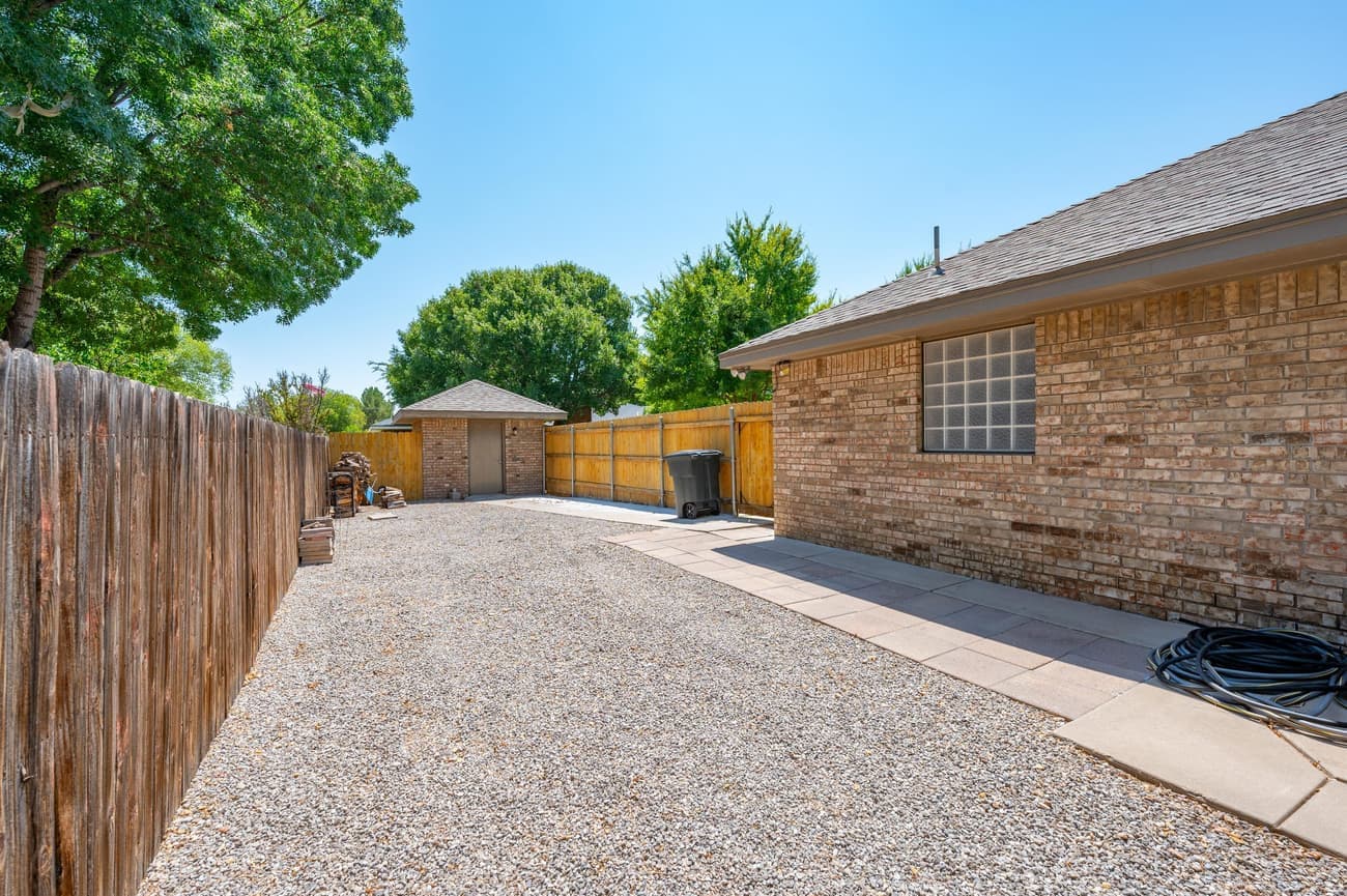 The graveled side yard behind a wooden gate, used as RV parking, running the length of the house to a storage shed.