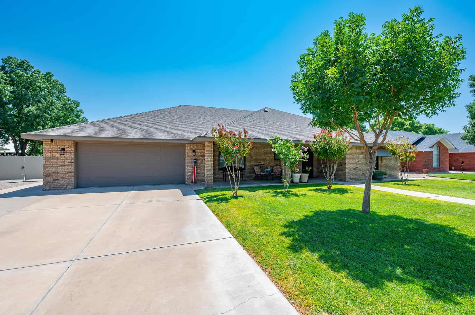 A wide concrete driveway running up to the two-car garage, with crepe myrtles and lawn alongside.