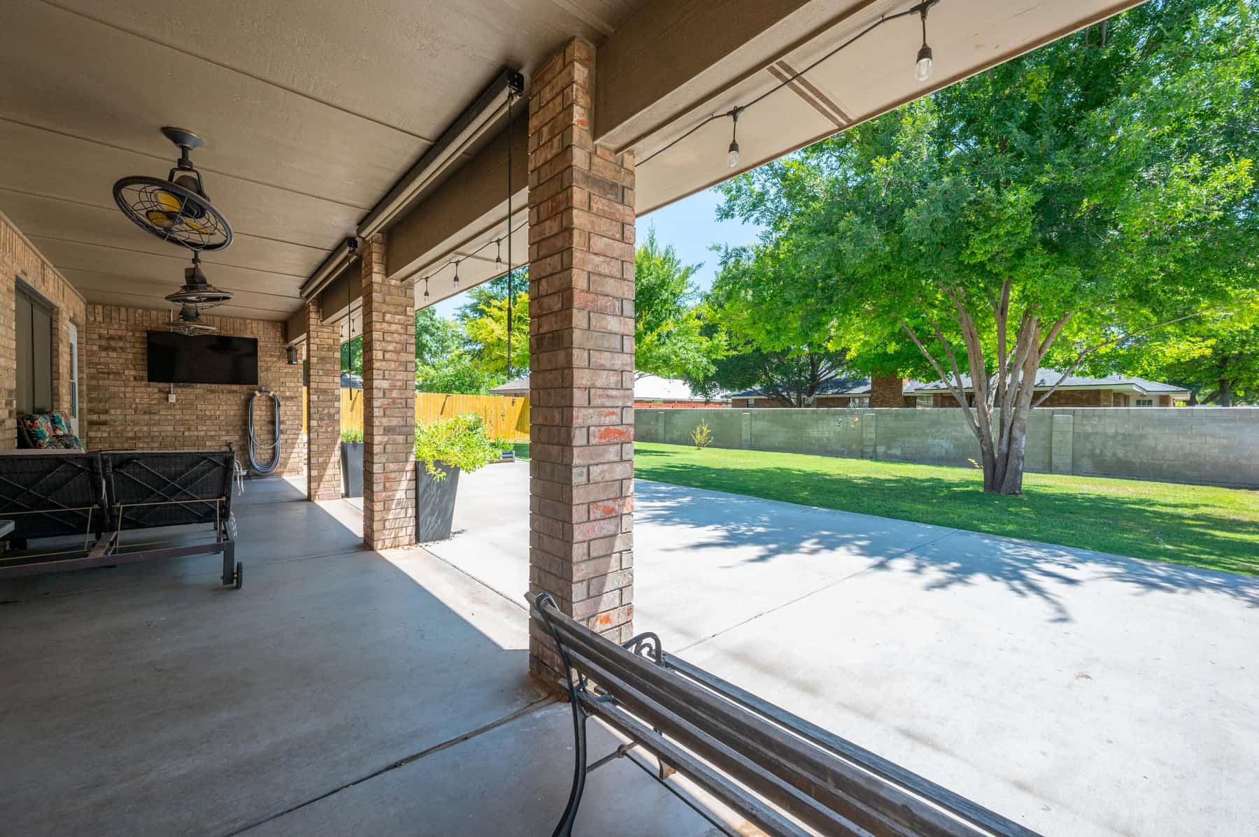The covered back patio with an outdoor television, ceiling fans, string lights and seating, looking out to the lawn.
