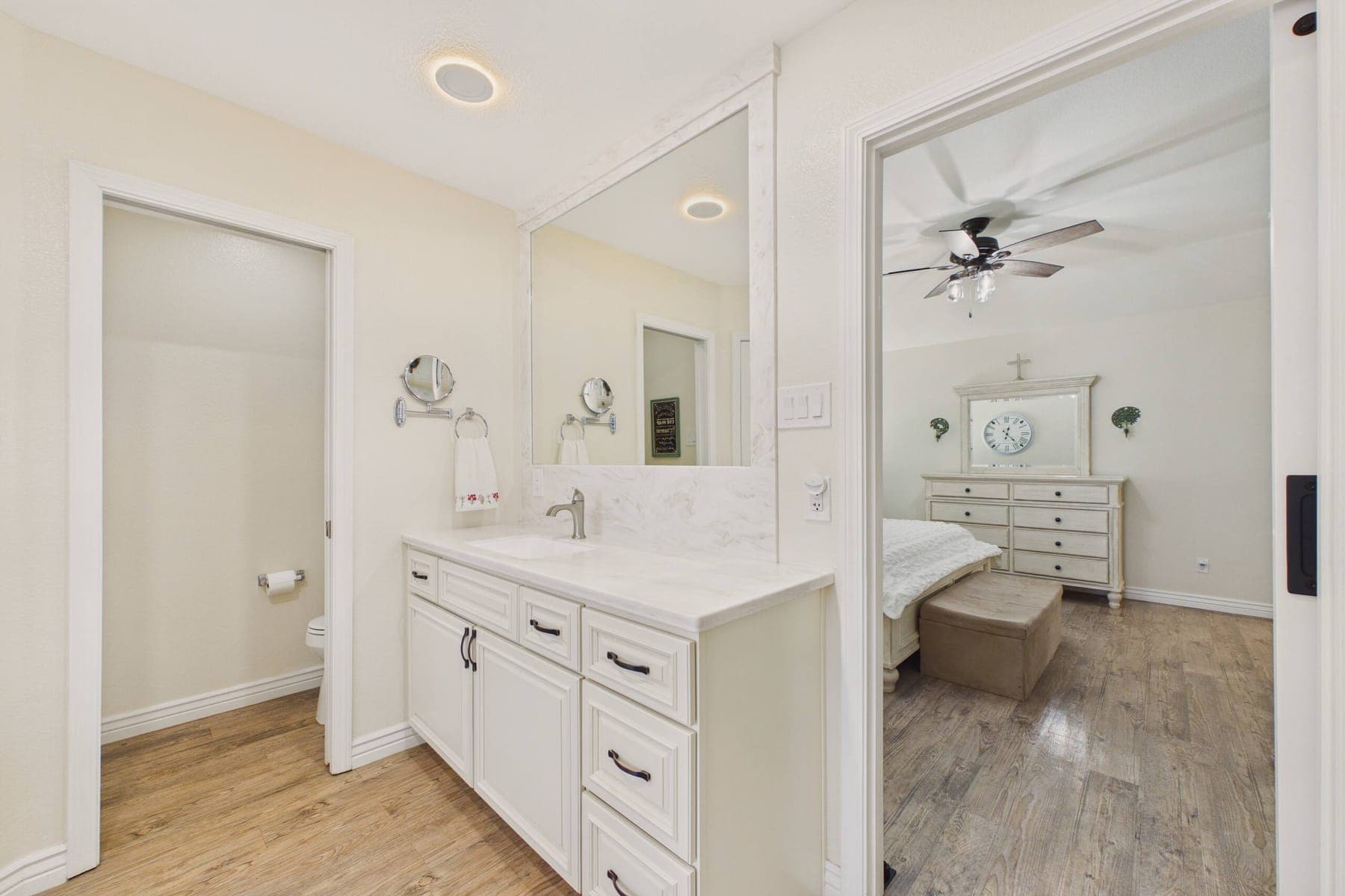 The first full bathroom: a long marble-look vanity with a framed mirror, a separate toilet room, and a doorway through to a bedroom.