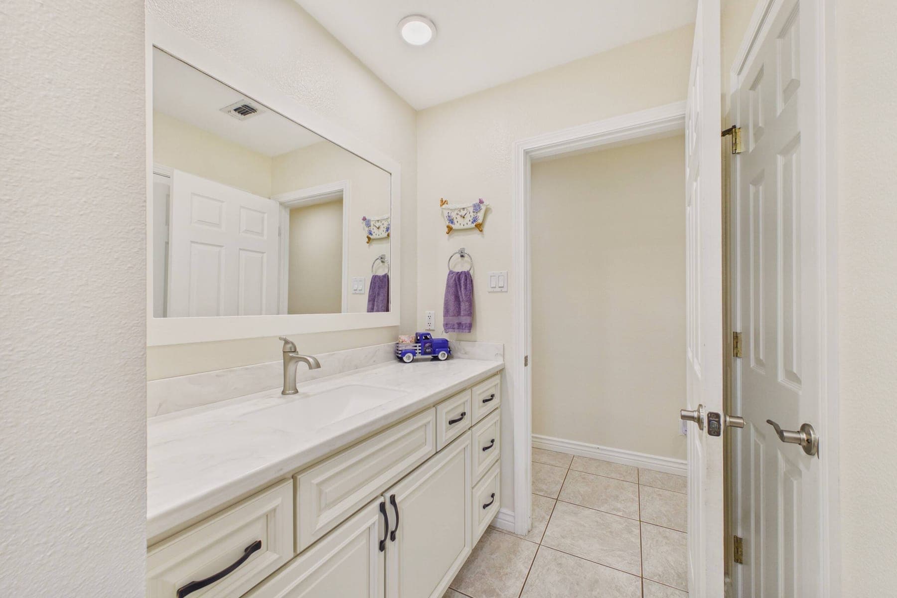 The second full bathroom: a marble-look vanity with cream cabinetry, a large framed mirror and tile flooring.